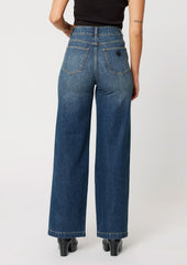 A woman wearing a pair of wide leg, high rise jeans in medium dark blue wash with seam down center leg.