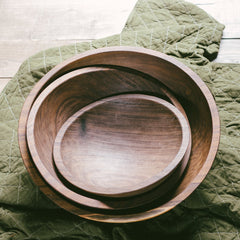 A set of three stacked black walnut wooden bowls on top of a green cloth.