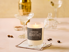 Candle labeled 'Espresso Martini' on a table with glasses and coffee beans.