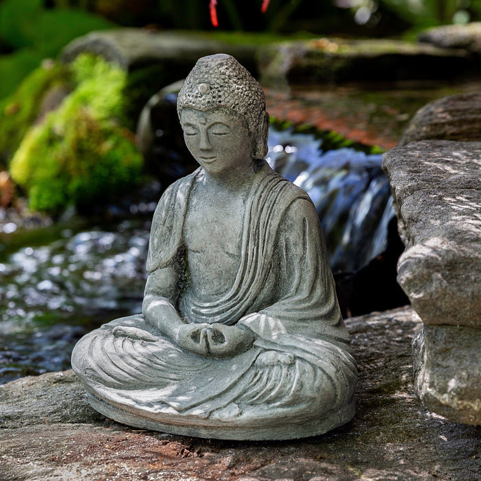 Sitting buddha in front of pond with maple tree branch