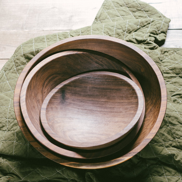 A set of three stacked black walnut wooden bowls on top of a green cloth.