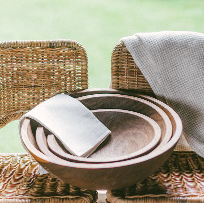 A set of three stacked black walnut wooden bowls on top of two side-by-side wicker chairs.