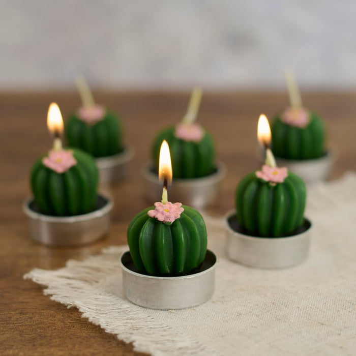 Cactus-shaped candles with pink flowers on top, arranged on a wooden surface.