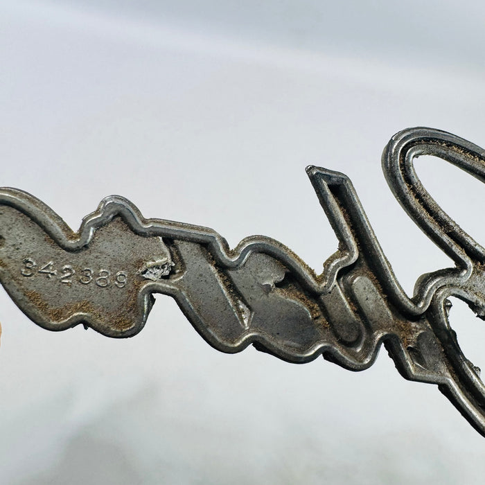 Close view of stamped 342389 part number on Chevrolet grille emblem