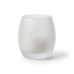 Frosted glass votive holder containing a white candle against a plain white background