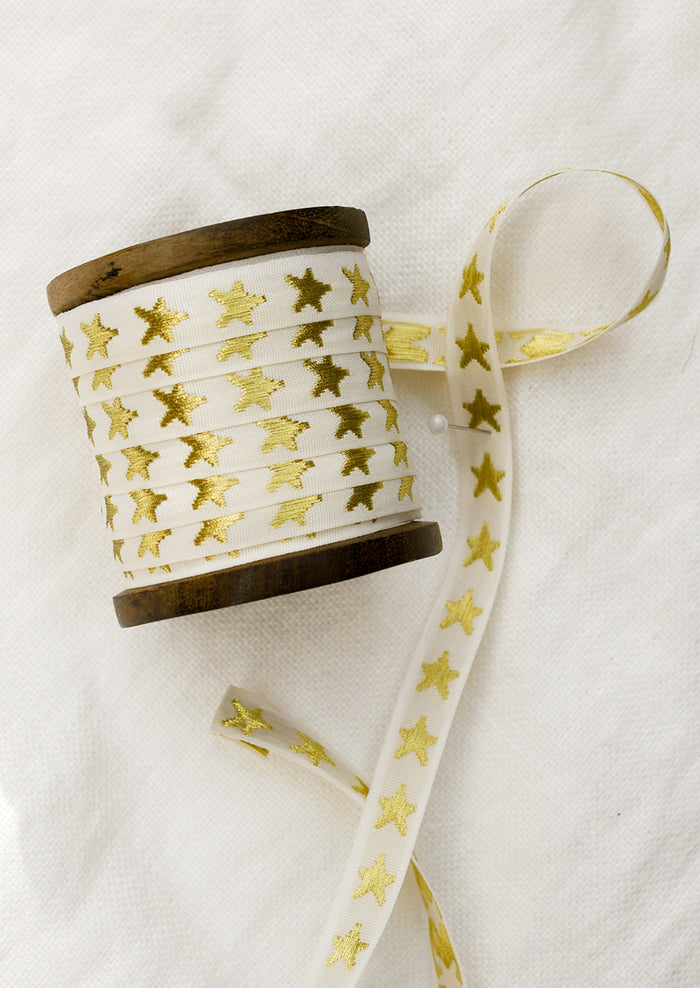 A walnut wood spool with cream ribbon with gold embroidered star pattern.
