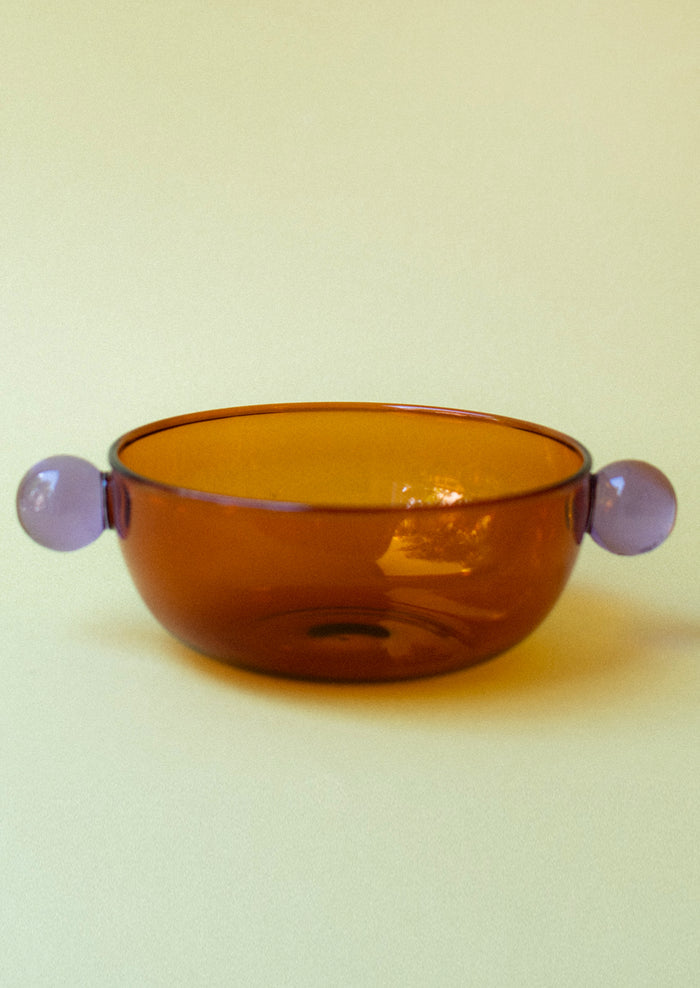 An amber glass bowl with lilac ball detail on sides.