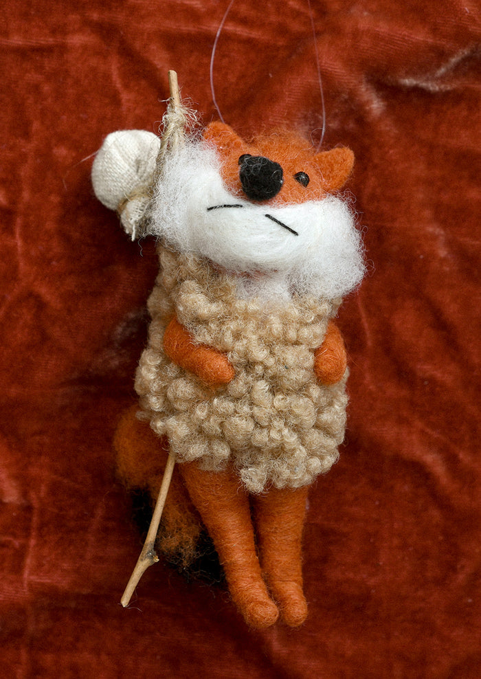 A felted wool ornament of fox carrying hiker pole.