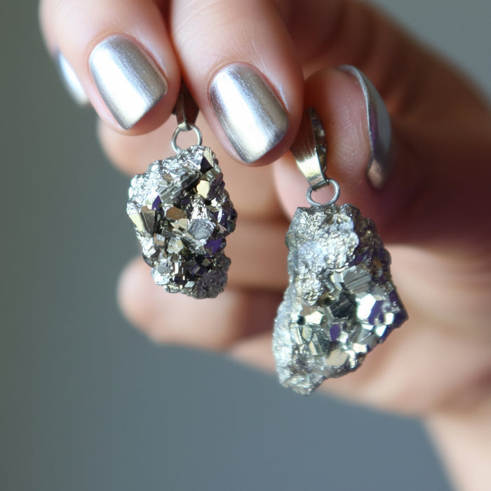 Geode-style Pyrite pendants held by a hand with purple nail polish against a neutral background
