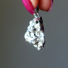 Close-up of a Pyrite pendant held by a hand with pink nail polish against a gray background