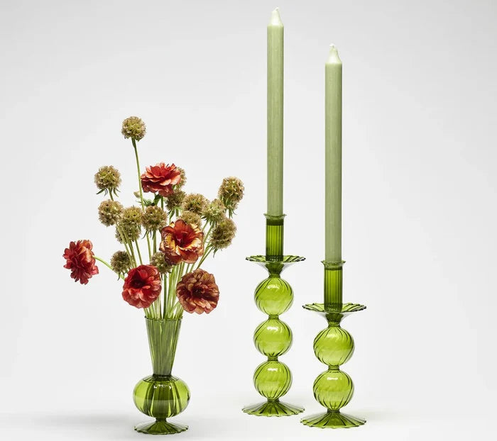 The Tess Bud Vase Set of 3 - Olive by Kim Seybert, featuring hand-blown green glass, is displayed with two matching candle holders and light green candles against a plain white background.