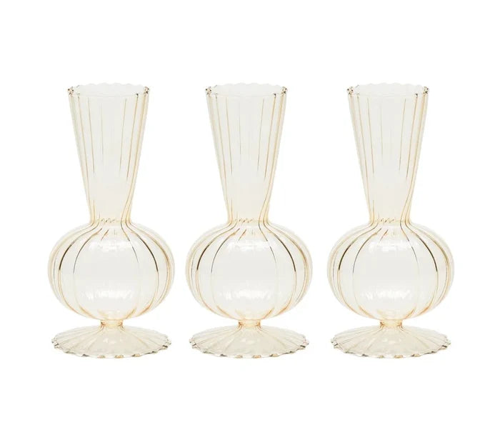 The Kim Seybert Tess Bud Vase Set of 4 in Champagne features identical translucent vases with round bases, fluted bottoms, narrow necks, and vertical ribbed lines, arranged side by side on a white background.