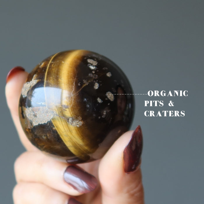 hand holding Den Muddy Earth Tigers Eye Sphere showing organic pits and craters