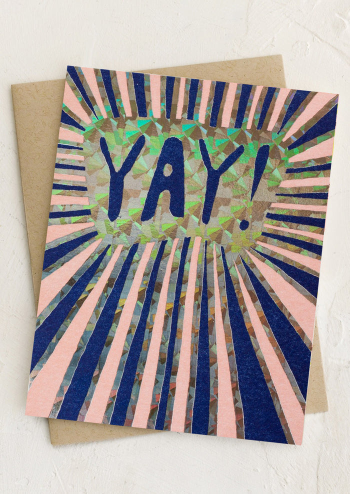 A greeting card with holographic sunburst print, text reads "YAY!".